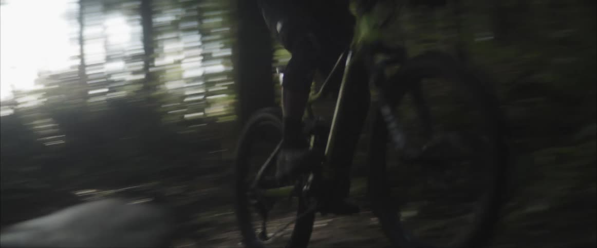 Person wearing helmet rides bike through woods past large rocks