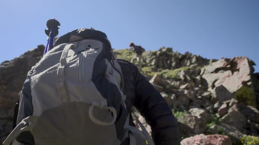 A person in a backpack climbs up a rocky hill