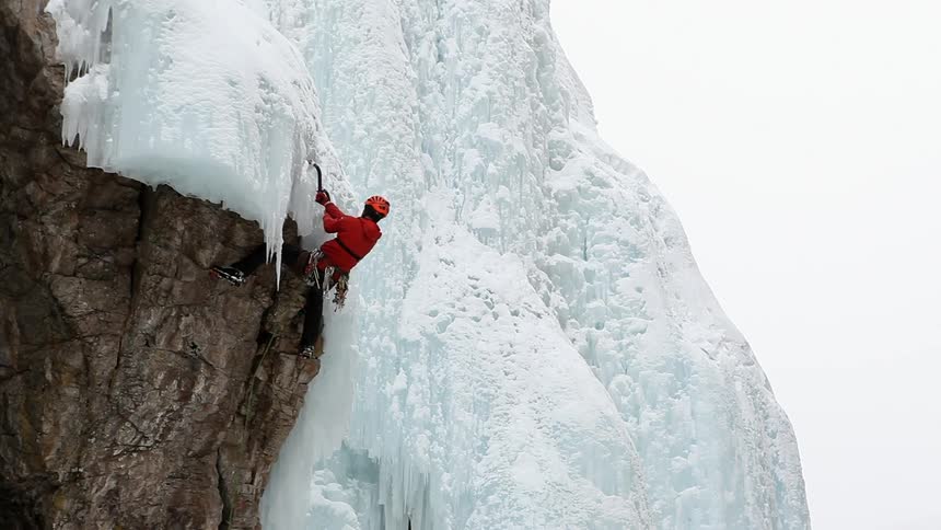 A rock climber secures his ice picks as he ascends an ice covered rock face