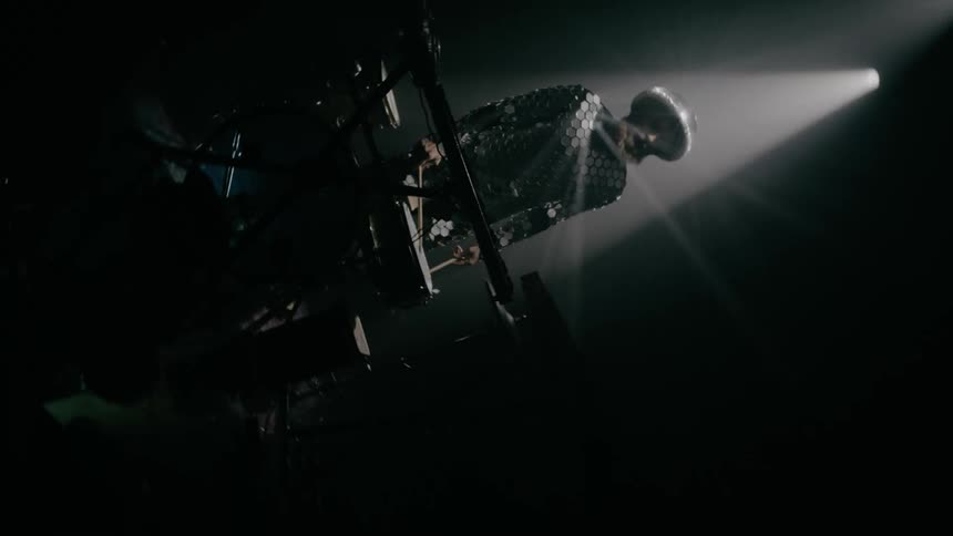 A man with drumstick standing in front of a drum set in a room with spotlights