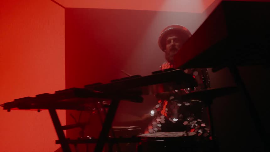 Male drummer energetically plays drums as wall and floor light panels change colors from reds to black