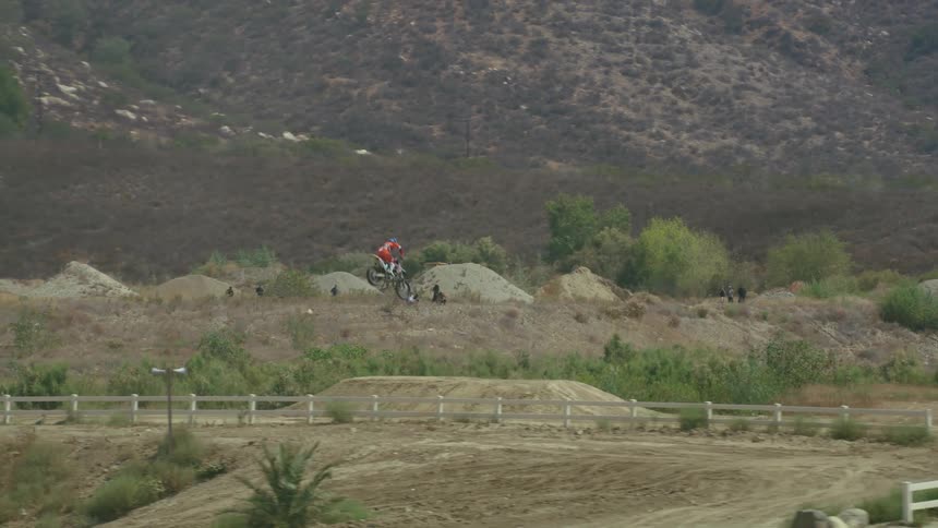 A person riding a dirt bike on an obstacle course with trees and a mountain range in the background