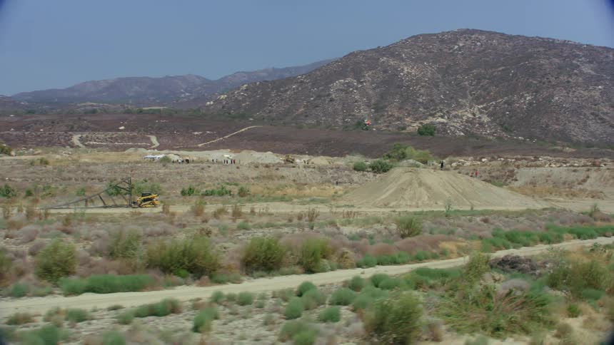 A person riding a dirt bike on an obstacle course with trees a mountain range the sky and clouds in the background