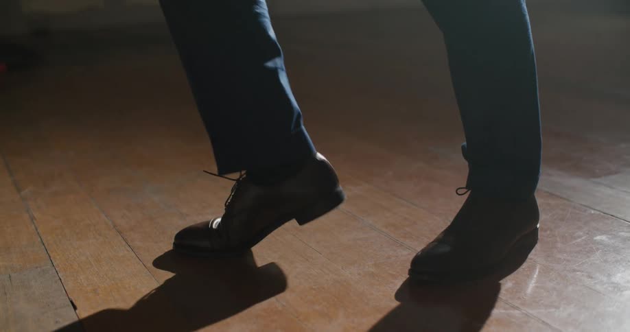 Person wearing leather taps heel and executes dance steps on wooden floor