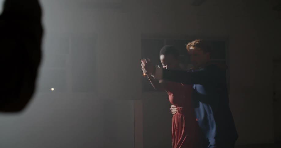 A man uses his smart phone and a long lens to record two people dancing in a brightly lit studio