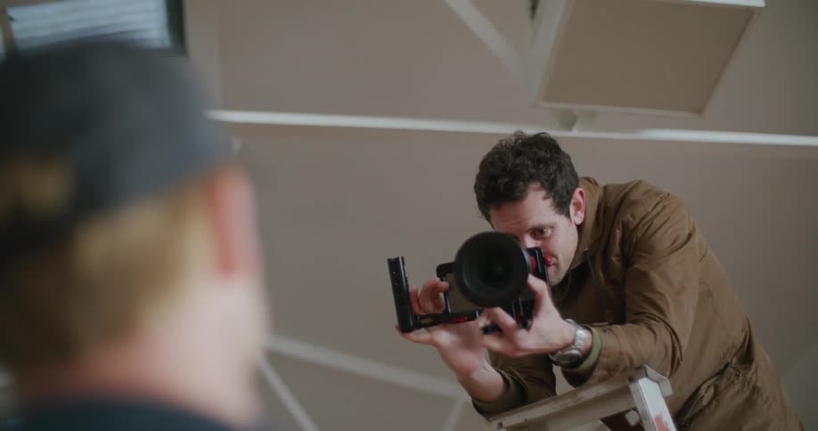 A man is aiming a camera on top of the ladder