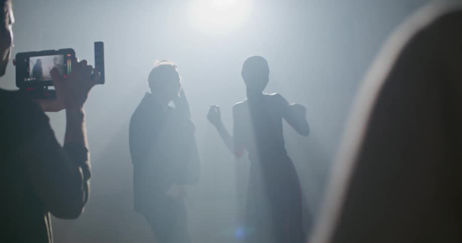 A man with a camera taking video of a man and woman dancing with a spotlight in the background