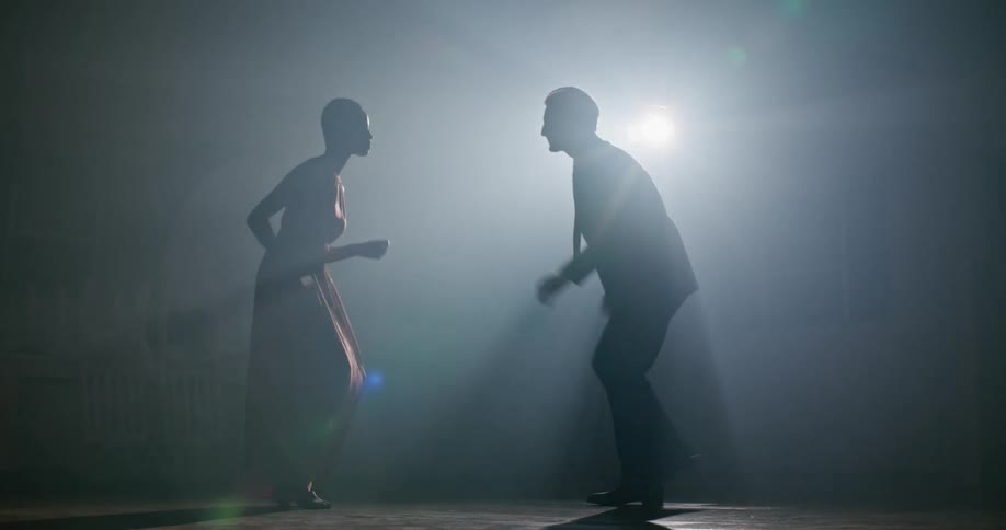 A silhouette of a man and woman in a room dancing with a spotlight in the background