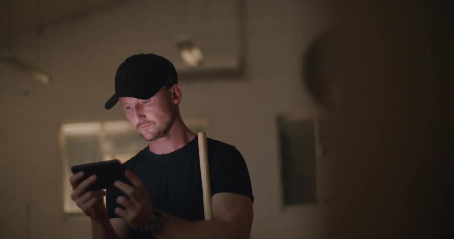 A man in a room looking at a smart phone with another person using a camera to video him