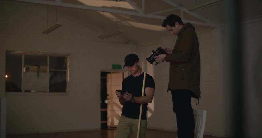 A man stands on a chair looking at a drone while another man holds a controller and a mop handle