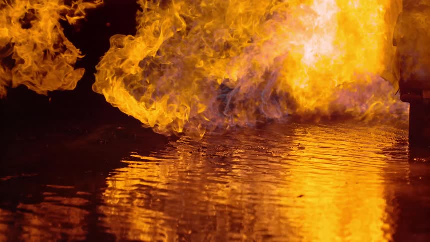 A large plume of flames is projected laterally above a large puddle of liquid