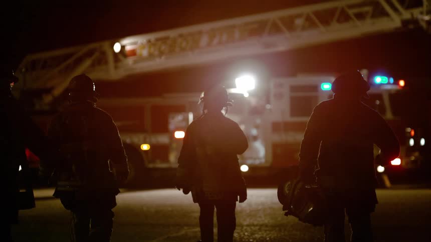 A group of firefighters walk towards a fire truck on a road at night
