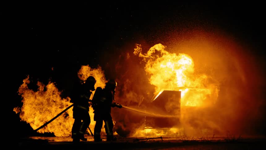 Two firefighters dousing a fire with water at night