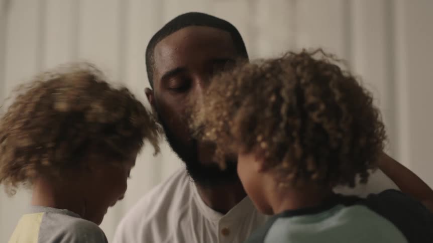Father holding his sons on his arms gently puts them on the floor inside a room at home