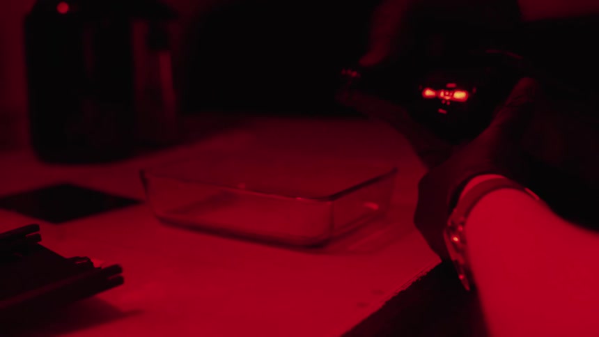 Person pours developing solution into glass container in darkroom