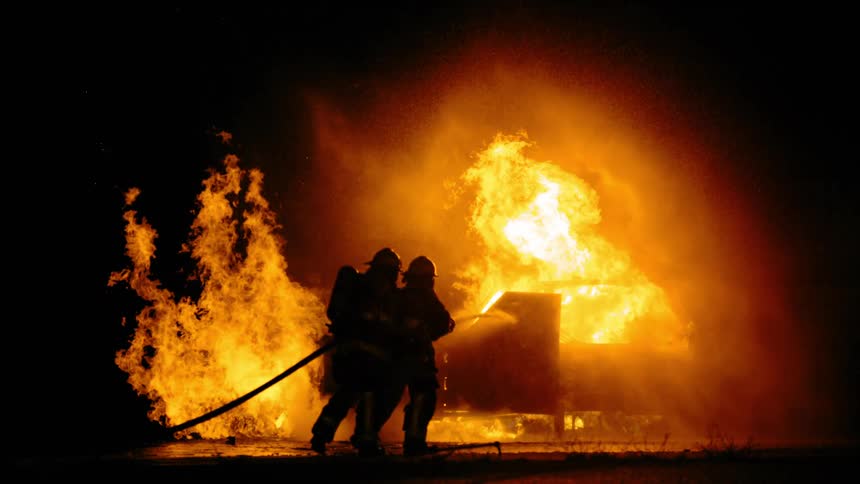 Firefighters extinguish burning car at night