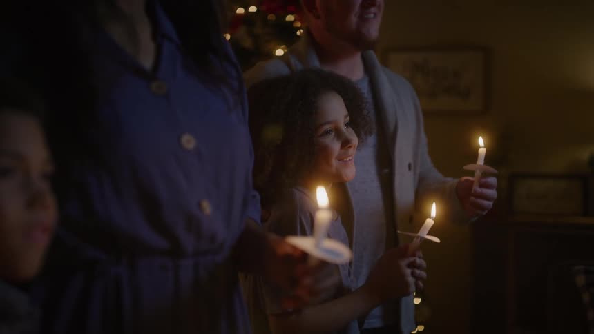 Family holds candles next to the christmas tree smiling at each other