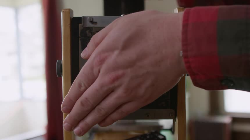 Hands load film into a vintage camera and operate with a remote