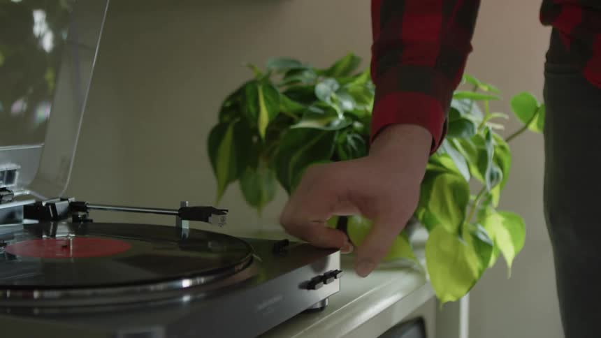 A man puts a record on a record player at home and plays it
