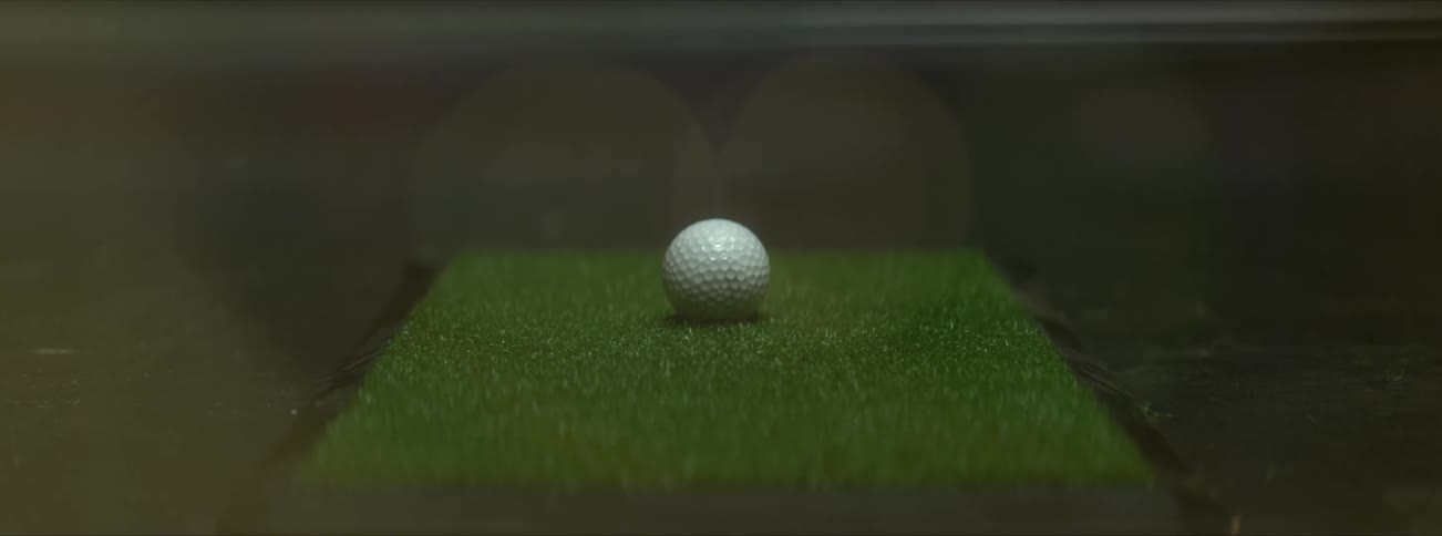A golf ball that is placed on a square of artificial grass is hit by a golf club