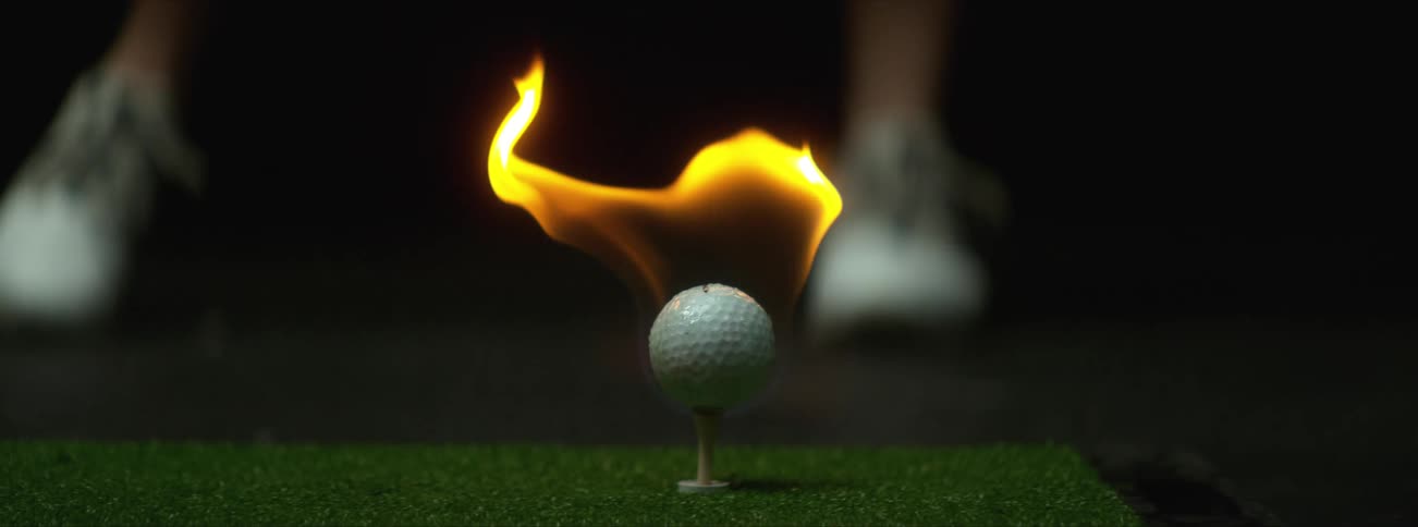 A person drives a golf ball that is on fire