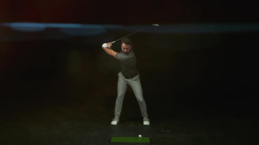 A man is practicing his golf swing at an indoor driving range