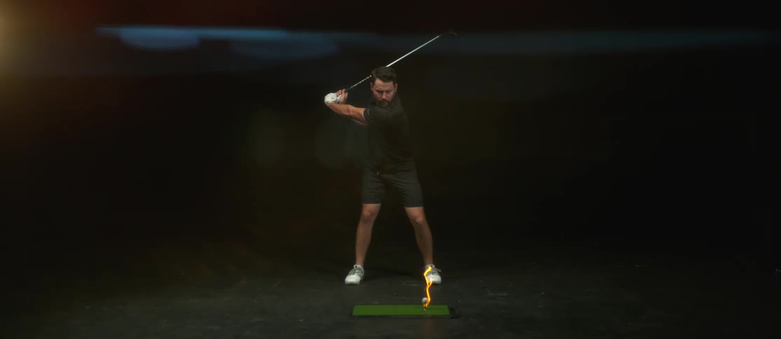A man with a golf club swinging at a golf ball on fire