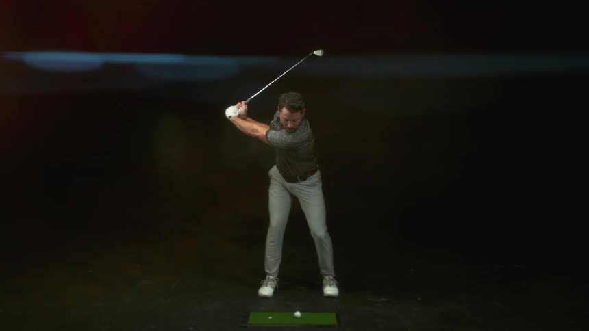 Man with beard grey polo shirt and pants plays golf on the dark background