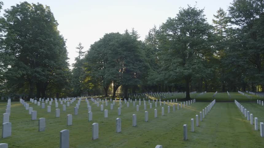 The sun peeks low through the trees surrounding a quiet and peaceful cemetary