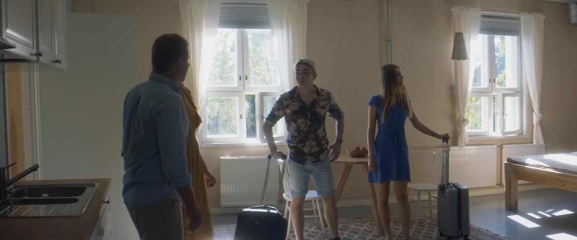 A young man and woman walk in to a room with suitcases as another couple show them the room