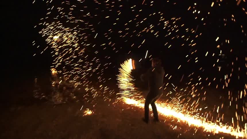 A man spins flames in a dark area
