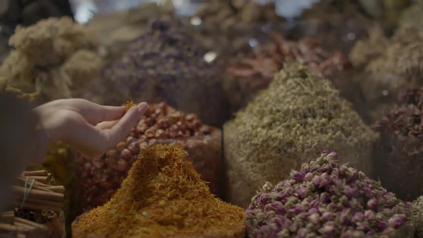A person grabs an ingredient from a large pile of herbs surrounded by other piles of herbs