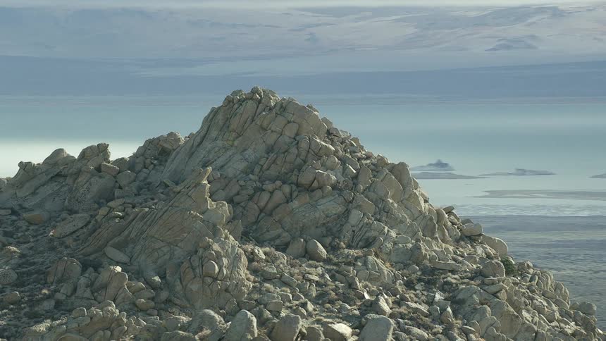A rocky cliff with a mountain range the sky and clouds in the background