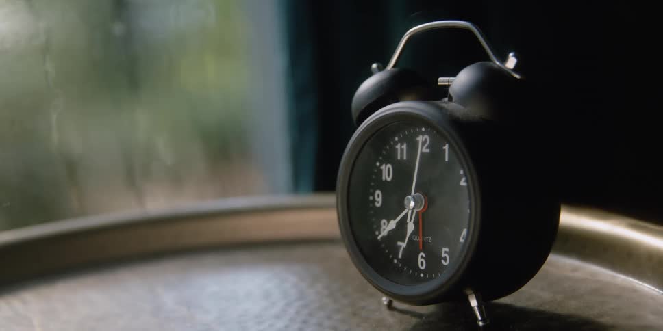 An old timey black clock ticks away on a tray near a misted window