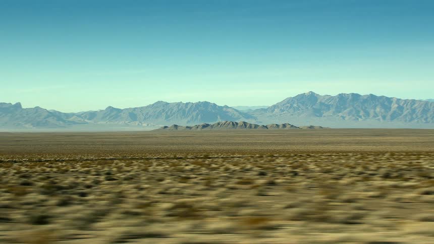 A vast arid shrub land with mountains looming in the distance on a clear day