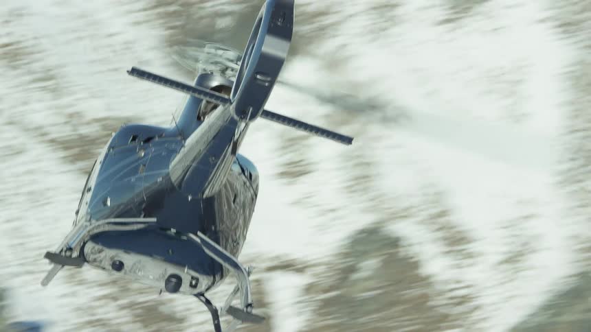 Tight shot of a flying helicopter in front of a mountain with light snow on it