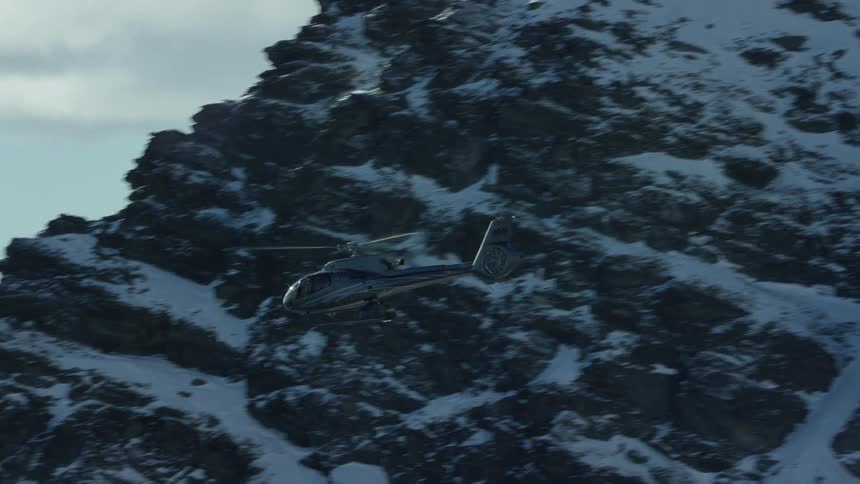 A helicopter flies in front of a snow capped mountain