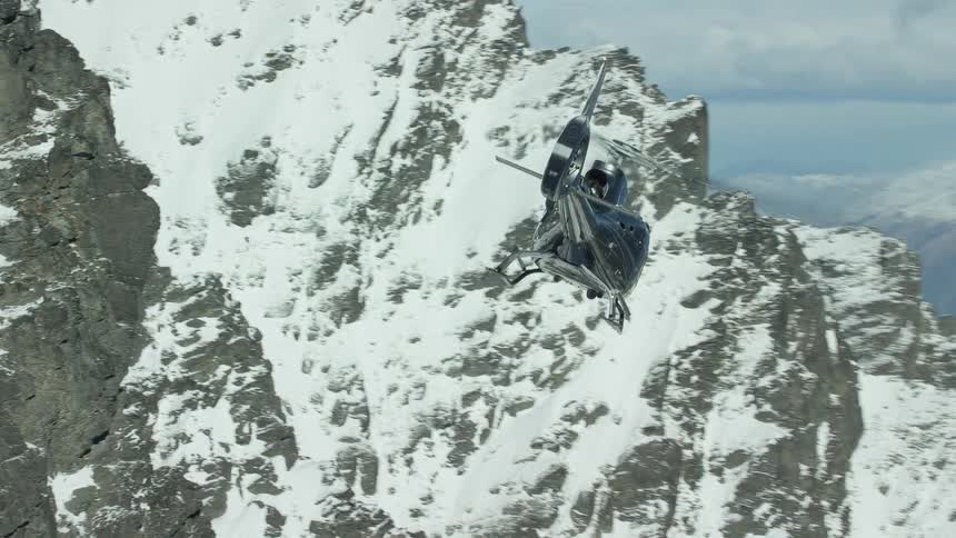 A helicopter flies over the high snow filled mountains