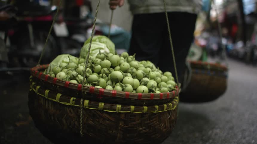 A person carries two heavy baskets of vegetables in a market
