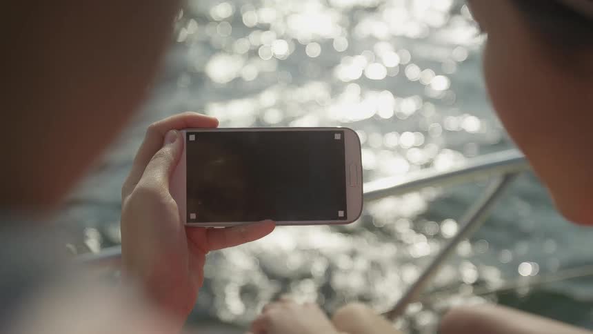 Two people on a boat looking at a smart phone with rippling water in the background