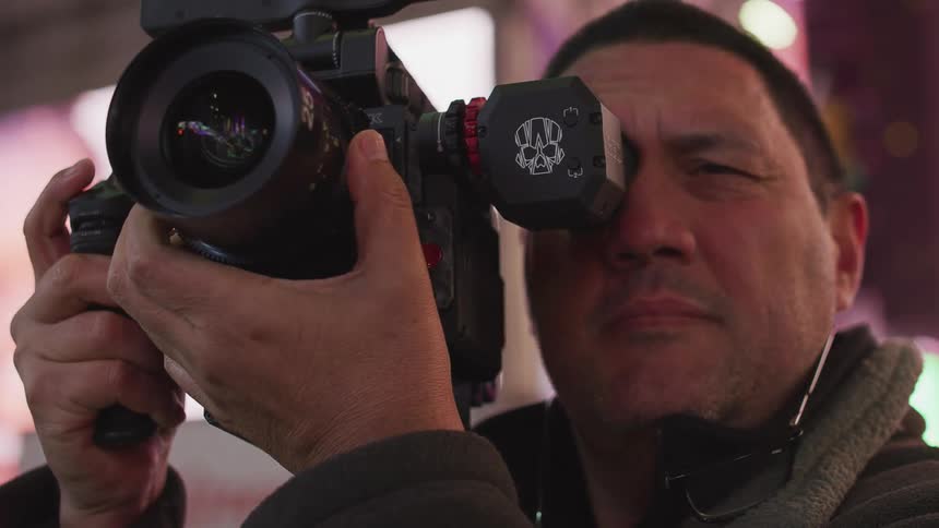 A man in a city taking pictures with a camera with buildings and signs in the background
