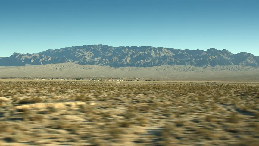 Bushes and shrubs in the plains badlands near a mountain range under a blue sky