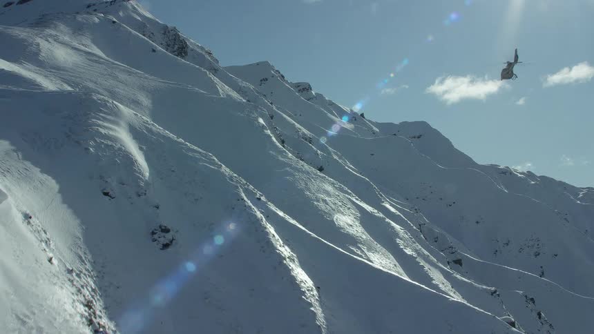 A view of a helicopter flying up near a mountain covered in snow