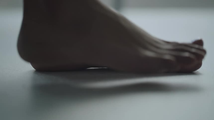 A person places one bare foot at a time onto the white floor