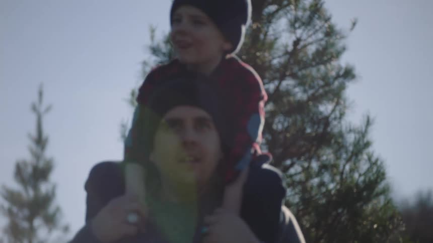 A man walks outdoors while a boy sits on his shoulders