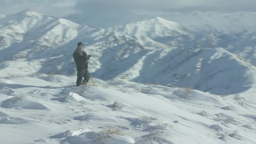 Photographer taking pictures atop the snow covered mountain top at winter