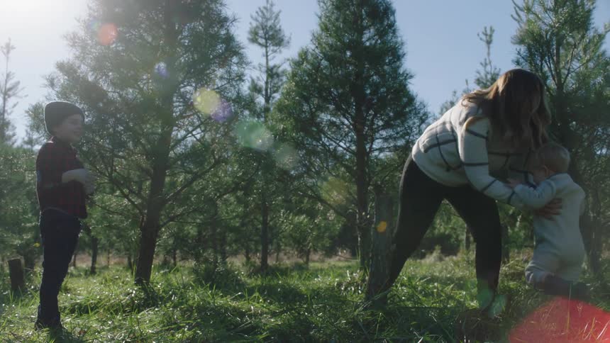 A mother walks to her adolescent son in a forest clearing and turns to lift up his younger sister