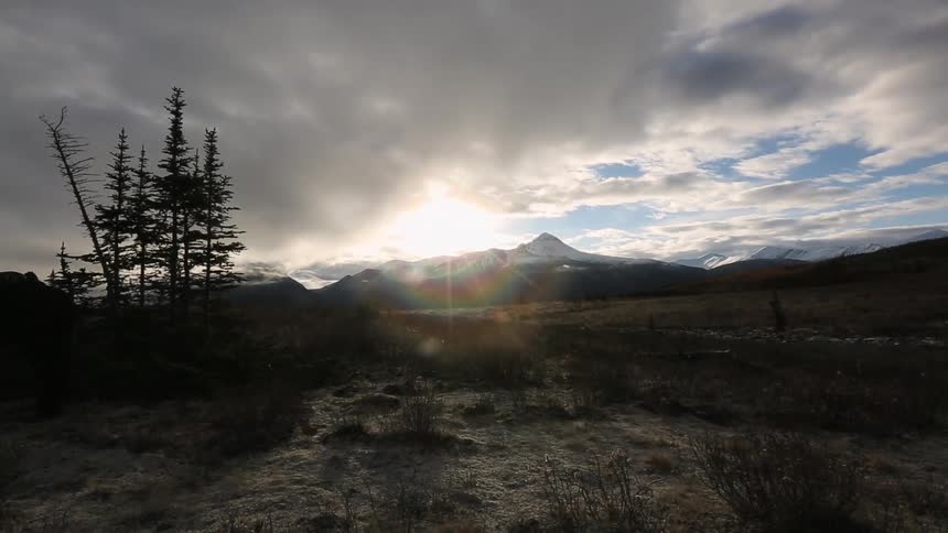 The sun shines brightly through the grayish clouds over a mountain