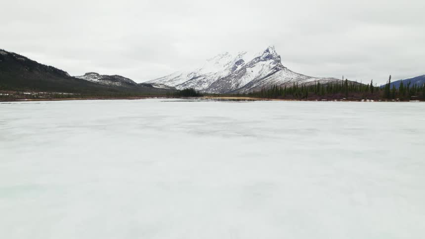 A frozen lake covered in ice with a mountain range the sky and clouds in the background
