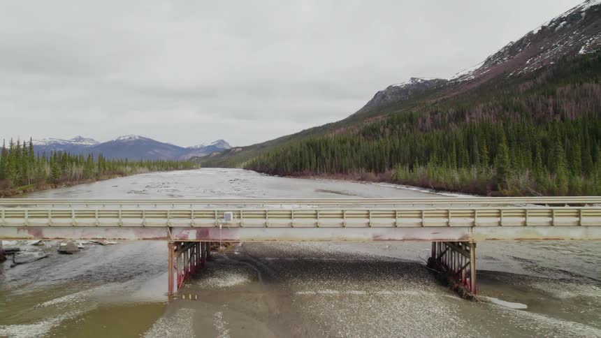 A bridge over a river with a mountain range the sky and clouds in the background